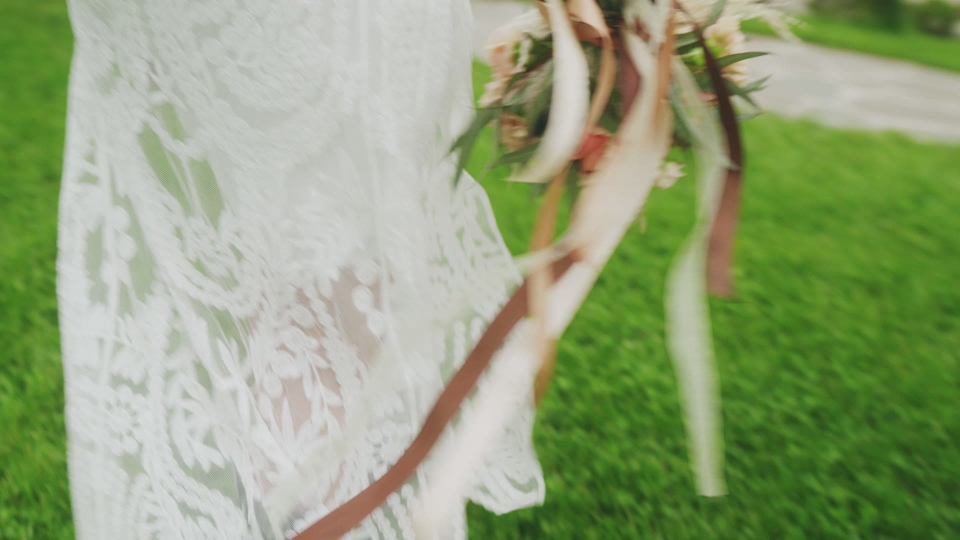 A bride's lace gown and ribboned bouquet drifting across the sunlit green lawn at Maroni Meadows
