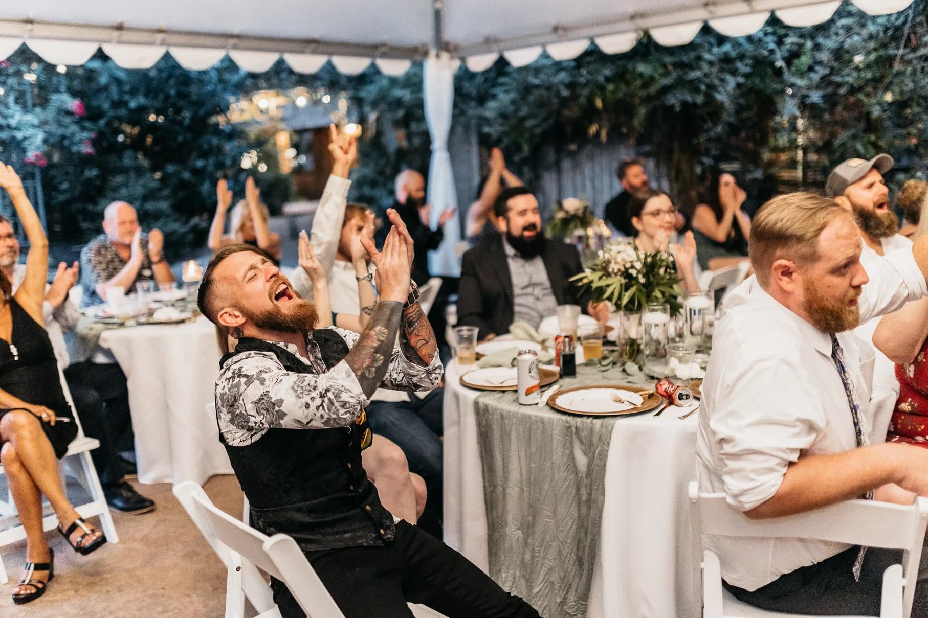 Guests cheering at reception tables under the tent, string lights and greenery overhead