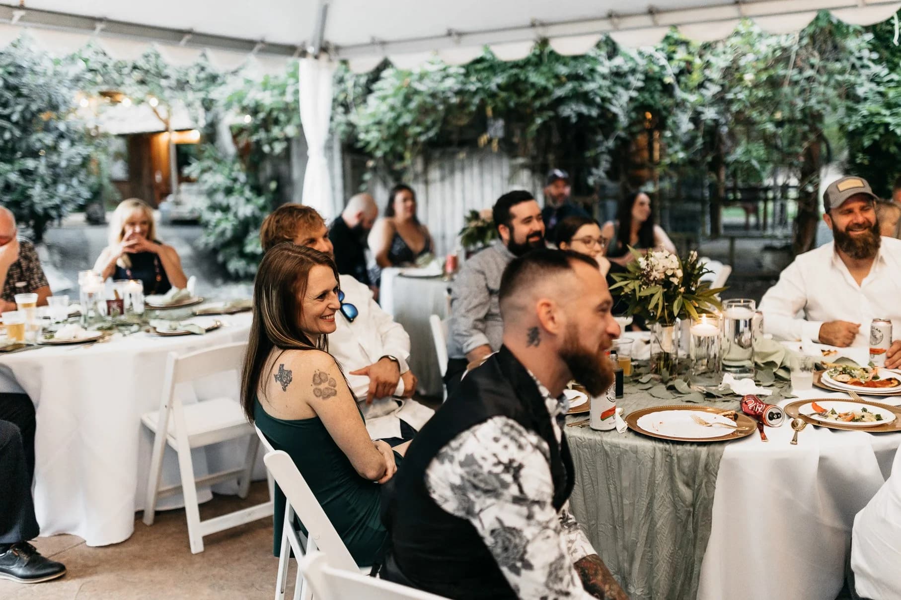 Guests seated at reception tables beneath the greenery-draped tent